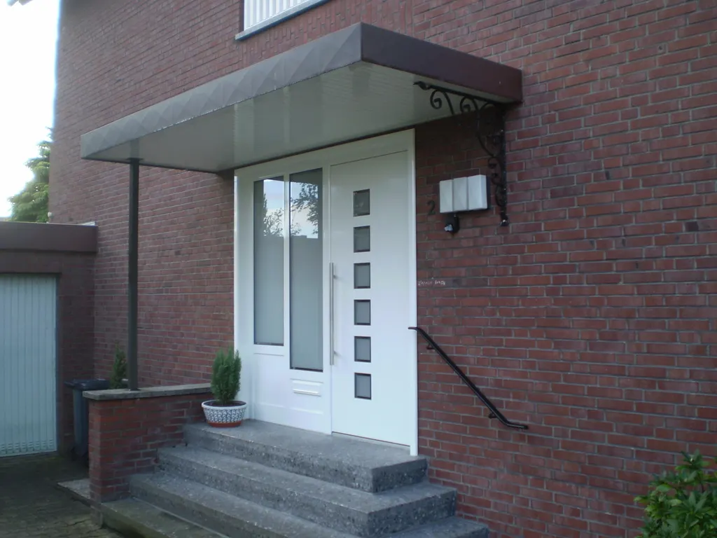 Weiße Haustür mit grauem Vordach und Handlauf