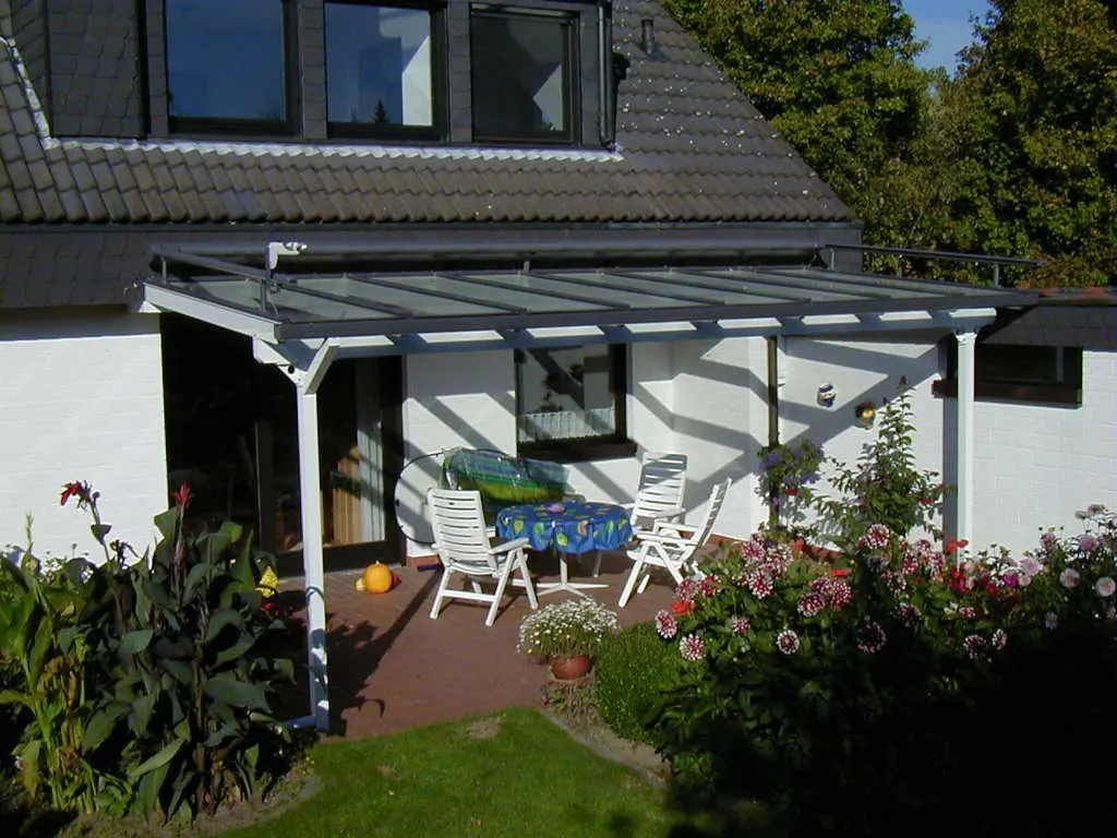 Terrassenüberdachung mit Glasdach an einem weißen Wohnhaus