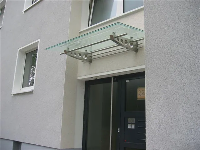 Glasvordach mit Edelstahlkonsolen an einer hellen Fassade
